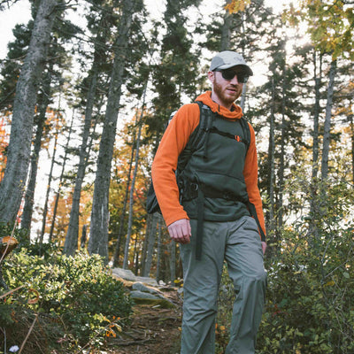Hiker wearing an orange and grey mid layer traverses the tall pines with the Hyperlite Mountain Gear Unbound 40 Pack