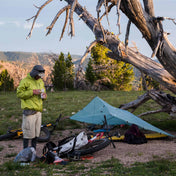 Camper eating beside their Hyperlite Mountain Gear Flat Tarp in Spruce Green in the woods