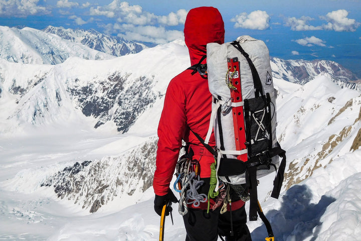 A man with a backpack standing on top of a snowy mountain.