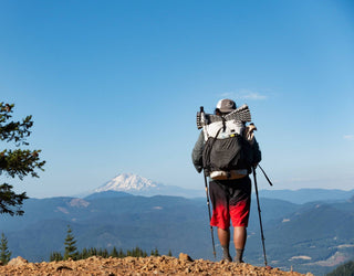A man with a backpack and hiking poles standing on top of a mountain.