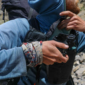 Hiker in a blue hoodie removes a camera from the Hyperlite Mountain Gear Camera Pod as it is strapped to their chest