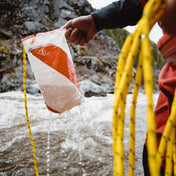 Someone demonstrating the use of the sewn drain holes on top and bottom of the Hyperlite Mountain Gear River Rescue Throw Bag