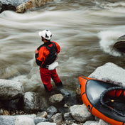 A kayaker stands on the edge of a raging river while using the Hyperlite Mountain Gear River Rescue Throw Bag