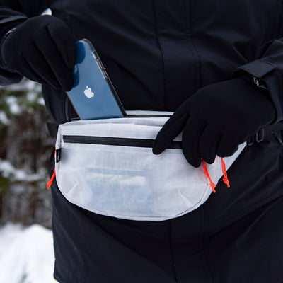 Front view of a person putting a cell phone in Hyperlite Mountain Gear's Versa in White