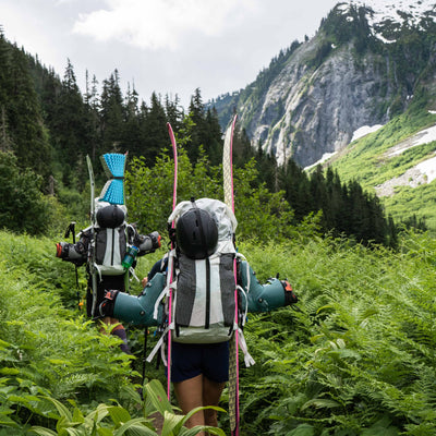 Hikers in the forest with skiis attached using the standard carry method on the Hyperlite Mountain Gear Headwall 55