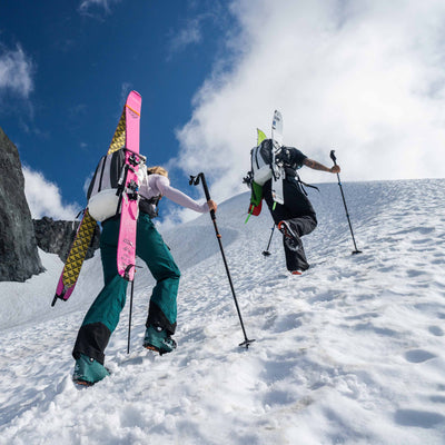 Two hikers ascending a snowy slope with trekking poles and skis on the Hyperlite Mountain Gear Headwall 55