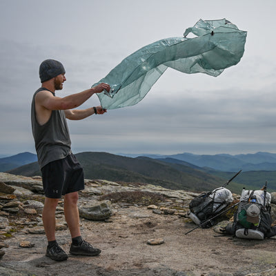 Hiker setting up Hyperlite Mountain Gear's Ground Cloth on a mountain