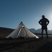 Front exterior view of Hyperlite Mountain Gear Shelters UltaMid 2 Half Insert inside white tent in a rocky landscape. A model stands next to the tent with hands on hips
