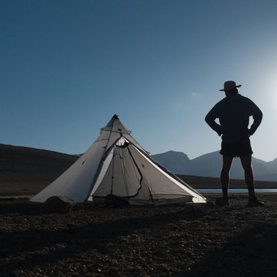 Front exterior view of Hyperlite Mountain Gear Shelters UltaMid 2 Half Insert inside white tent in a rocky landscape. A model stands next to the tent with hands on hips