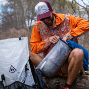 Hiker stuffing a Hyperlite Mountain Gear's 10L Side Entry Pod with clothing