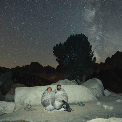 Two campers bundled up in their Hyperlite Mountain Gear 20-Degree Quilts lay underneath the stars