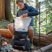Hiker sitting on a log packing up the Hyperlite Mountain Gear Unbound 40 Pack in the forest