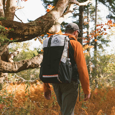 Hiker traverses through green and orange foliage wearing the Hyperlite Mountain Gear Unbound 40 Pack in White