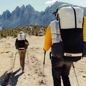 Two hikers in a clearing with trekking poles toting their fully packed Hyperlite Mountain Gear Unbound 40 packs
